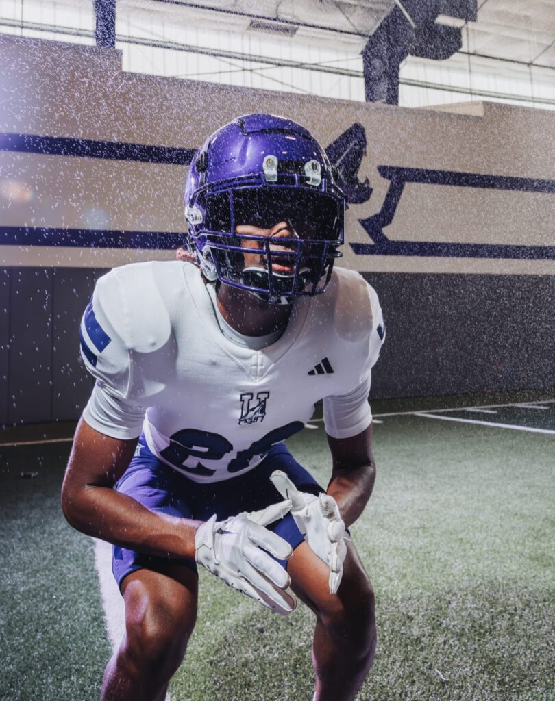 Football player in a purple helmet and white jersey crouched in a ready stance