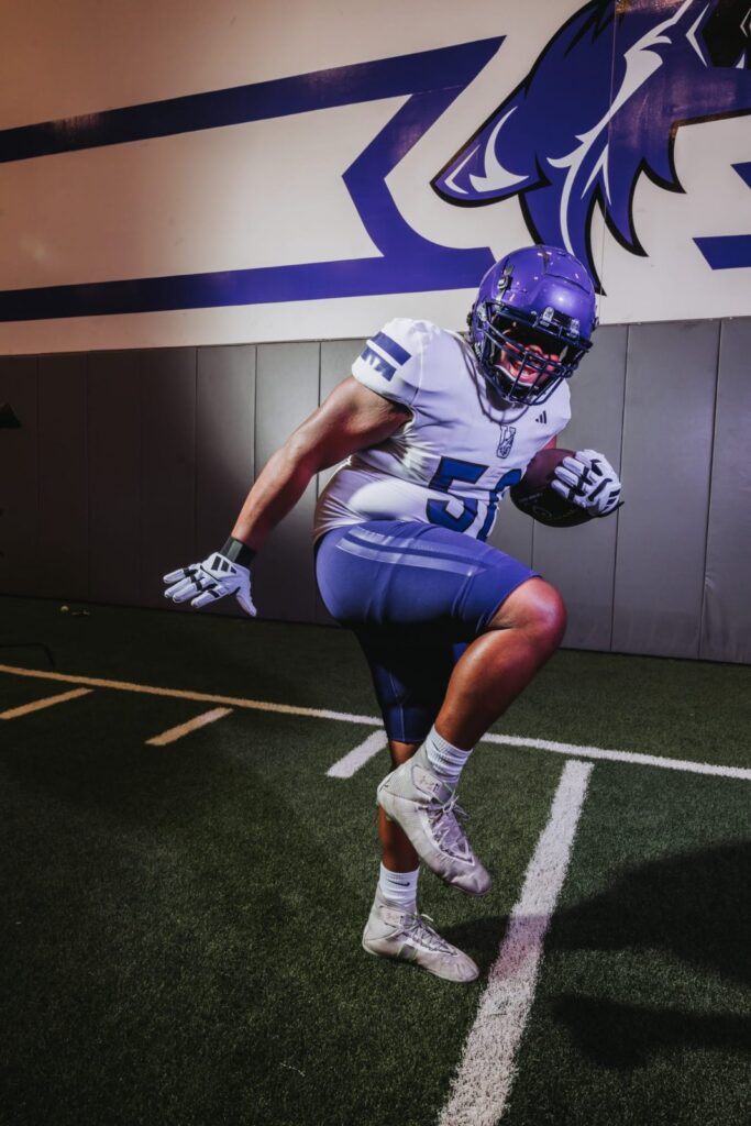 Football player in a purple helmet leaping across an indoor turf field