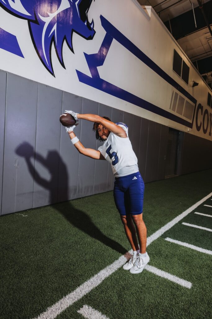 Football player reaching for a ball beside a wall painted with the team mascot
