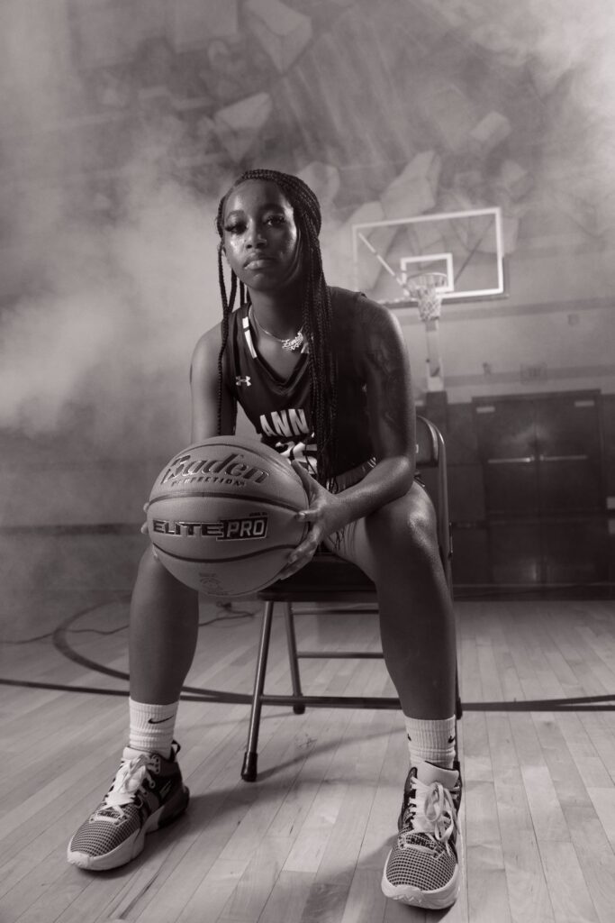 Black and white portrait of a basketball player seated with a ball in a smoky studio