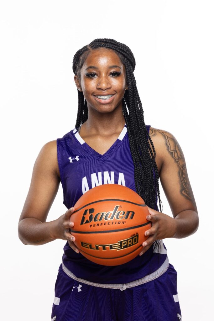 Girls basketball player in a purple Anna jersey holding a basketball against a white background