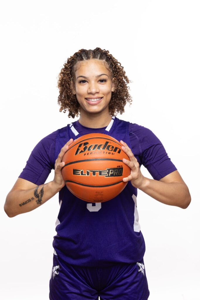 Girls basketball player in a purple jersey holding a basketball against a white background
